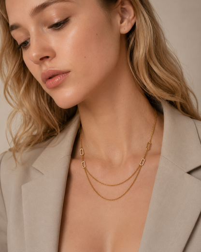 The Mora NECKLACE worn from a downward angle over a beige blazer, showing the layered pave links and draped chain along the collarbone.