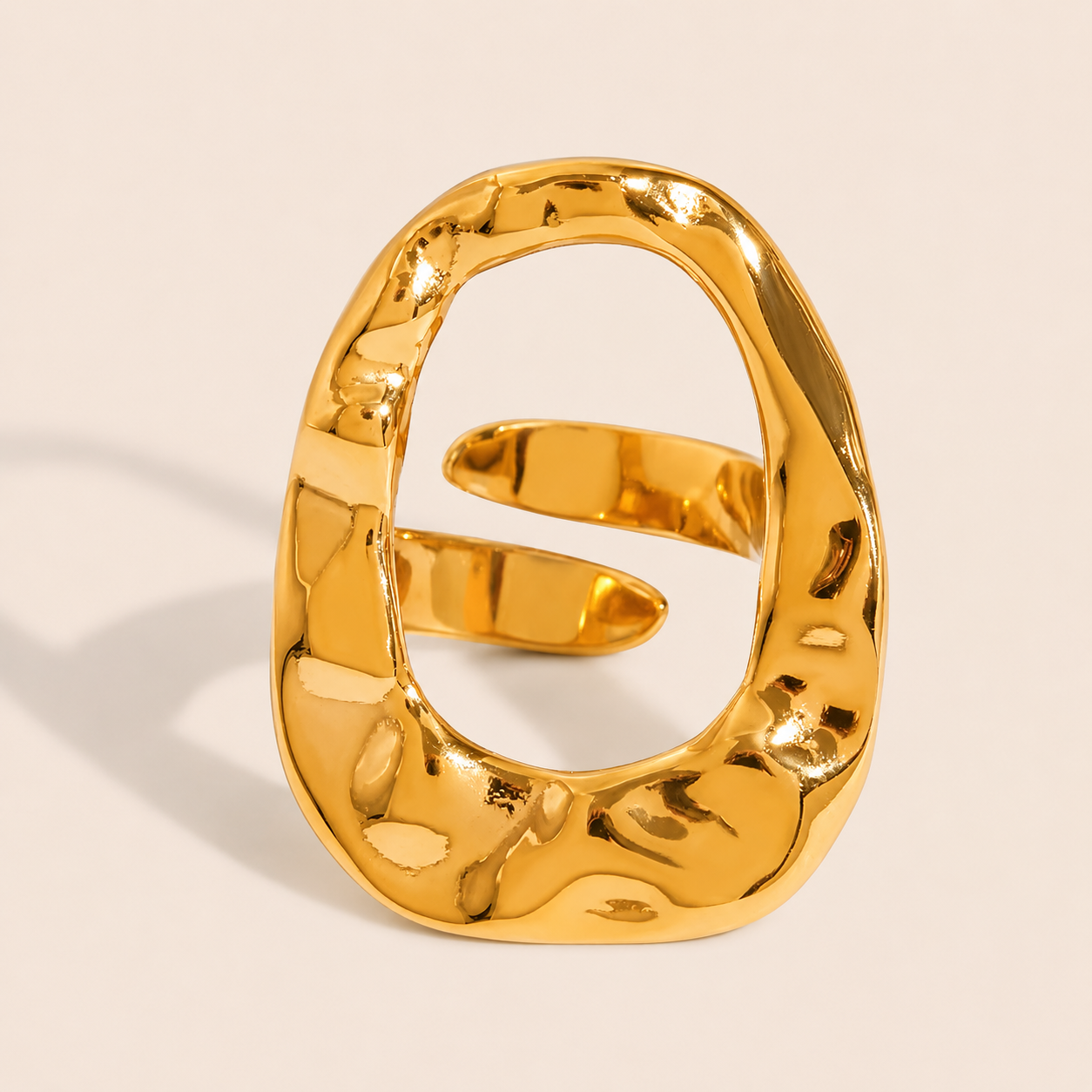 Gold hammered-texture ring with an open oval face wrapped by a thin overlapping coil, on a cream backdrop — Folie à Trois Move Over RING.