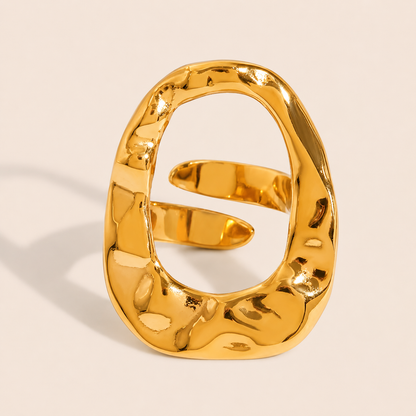 Gold hammered-texture ring with an open oval face wrapped by a thin overlapping coil, on a cream backdrop — Folie à Trois Move Over RING.