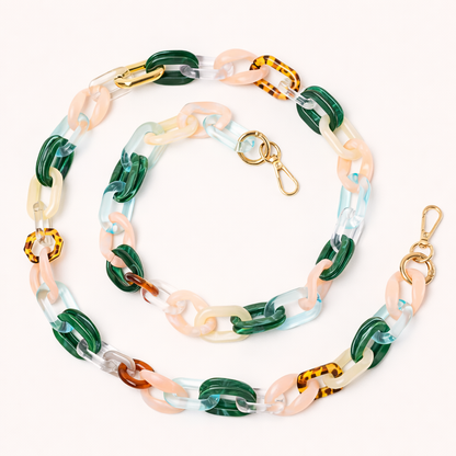 A coiled acrylic link phone chain in green, pink, clear, and tortoiseshell tones with a gold clasp, shown on a cream background.