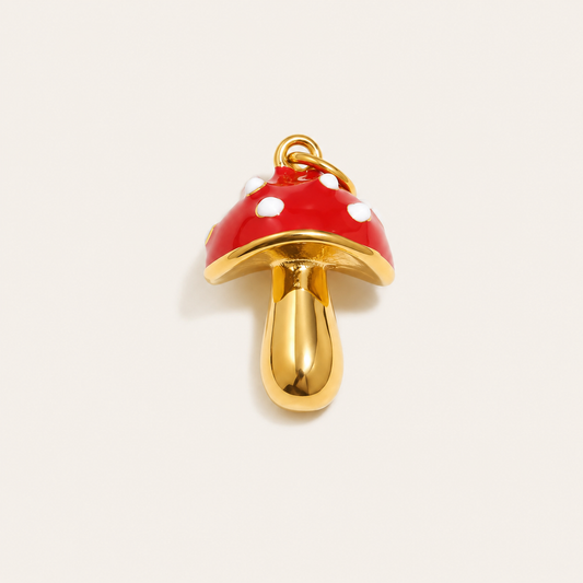 The Mushroom CHARM in gold, a red enamel toadstool pendant with white polka dots, shown in close-up studio photography on cream.