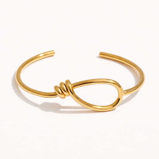 Neeve BRACELET gold open cuff with a knotted teardrop loop detail, studio flat-lay on a white background.
