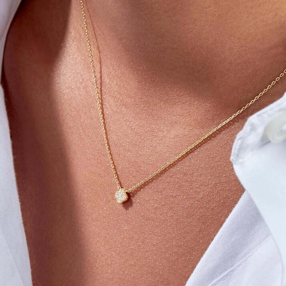 The Nessa NECKLACE in gold worn at the neckline, the sparkling clover cluster pendant above a white button-up shirt.