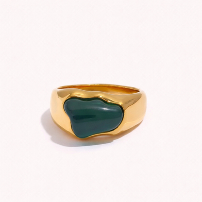 Gold signet-style New Fashion RING set with an irregular green cabochon stone, shown at an angle on a cream backdrop.