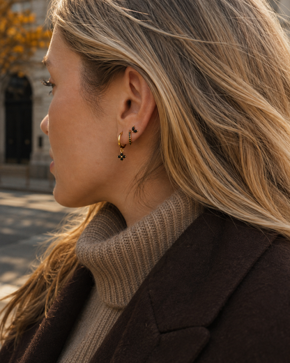 Model wears the Folie à Trois New Perspective SET in black onyx along the ear, a stud paired with a dangling clover hoop, styled outdoors.