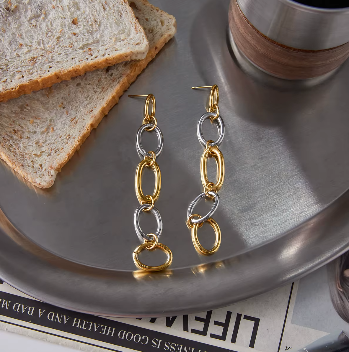 The No Apologies EARRINGS lie on a marble tray beside toast, showing their two-tone oval link chain.