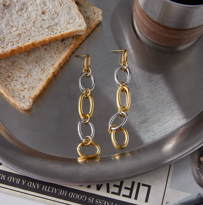 The No Apologies EARRINGS lie on a marble tray beside toast, showing their two-tone oval link chain.