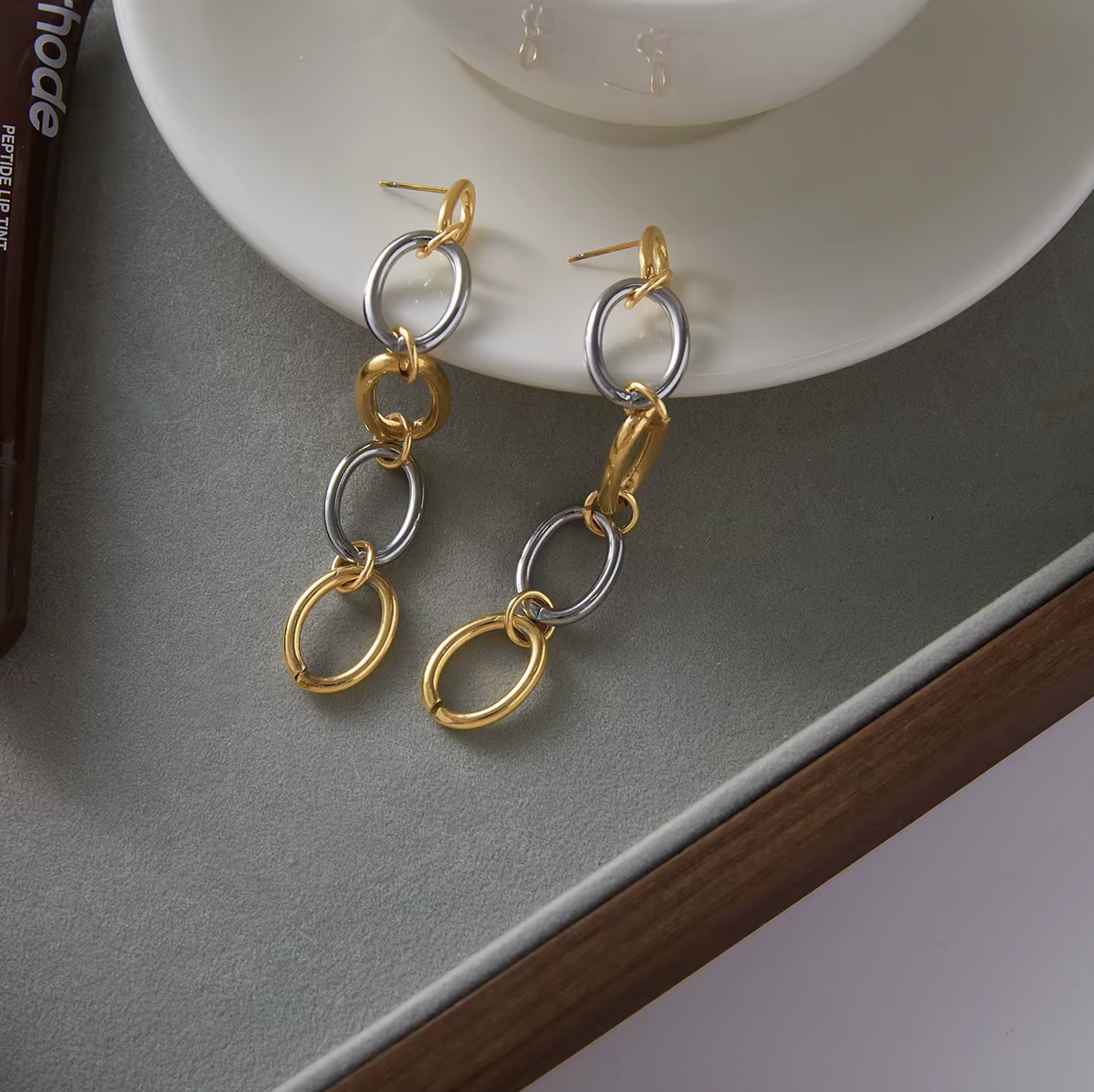 The No Apologies EARRINGS rest beside beauty products on a tray, showing their gold and silver link drop.