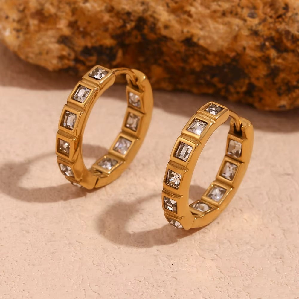 No Filter Earrings in gold styled against a textured stone backdrop, showing the square crystal hoops up close.