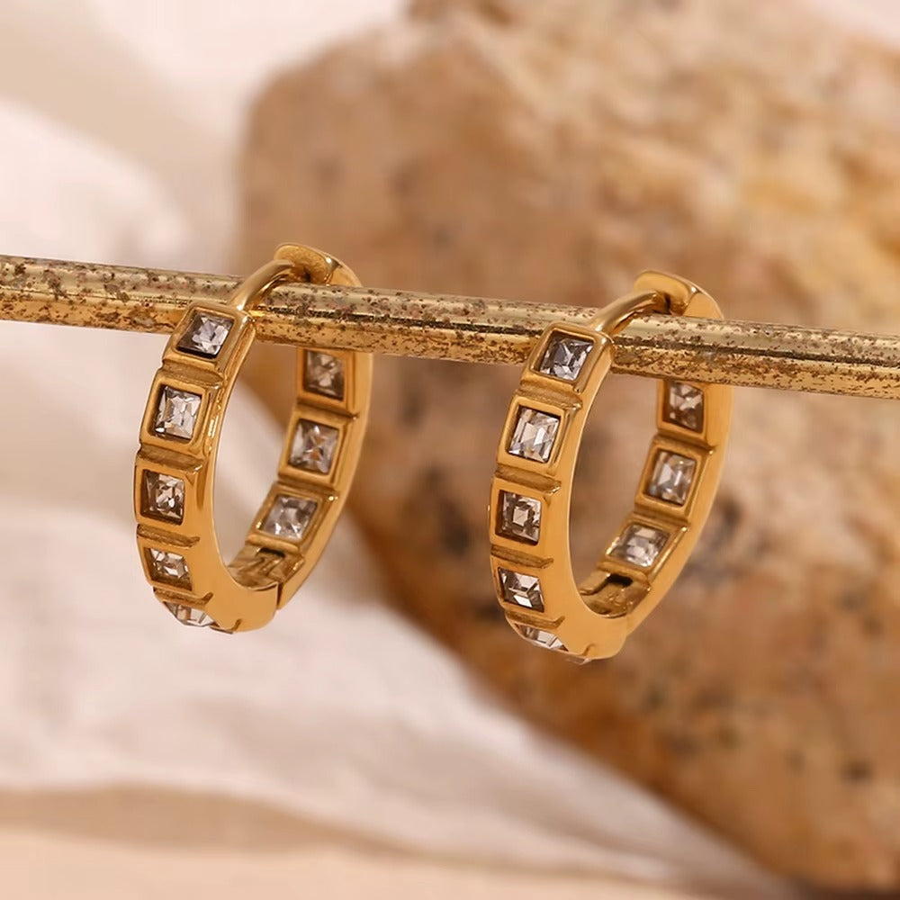 No Filter Earrings in gold hanging from a bar with soft linen fabric behind, square crystals catching the light.