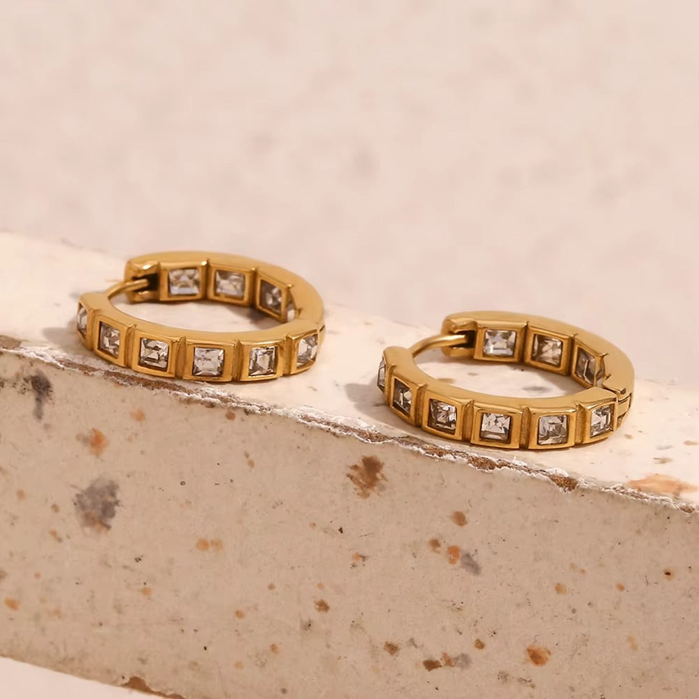 No Filter Earrings in gold resting on a stone ledge against a marbled cream background, crystals sparkling.