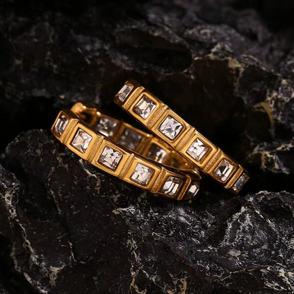 No Filter Earrings in gold resting on dark textured rock, the square-cut crystal hoops catching the light.
