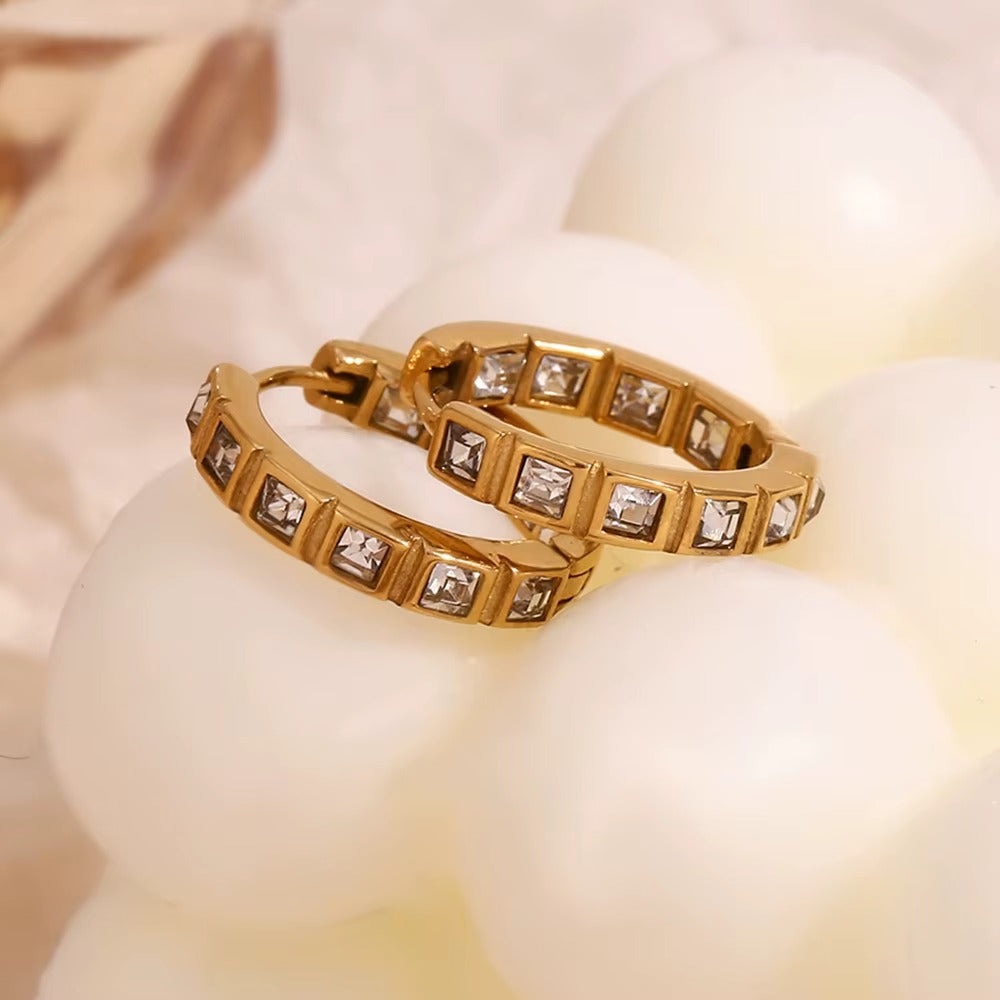 No Filter Earrings in gold resting on pearls with soft draped fabric, showing the square crystal hoop design.