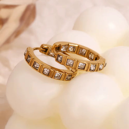 No Filter Earrings in gold resting on pearls with soft draped fabric, showing the square crystal hoop design.