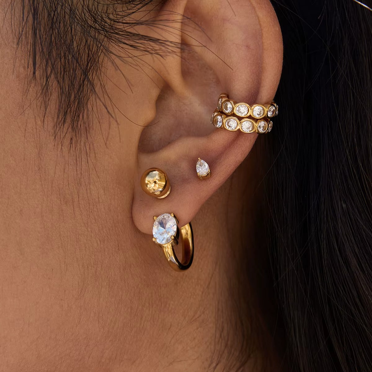 Nomad ear cuff worn stacked at the top of the ear alongside a gold ball stud and an oval crystal hoop earring.
