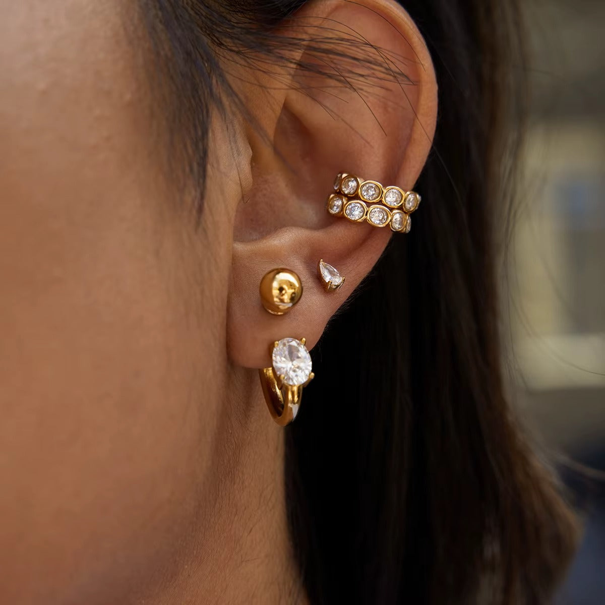 Nomad crystal ear cuff worn on the upper ear, styled together with a ball stud and an oval crystal hoop from another angle.