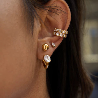 Nomad crystal ear cuff worn on the upper ear, styled together with a ball stud and an oval crystal hoop from another angle.