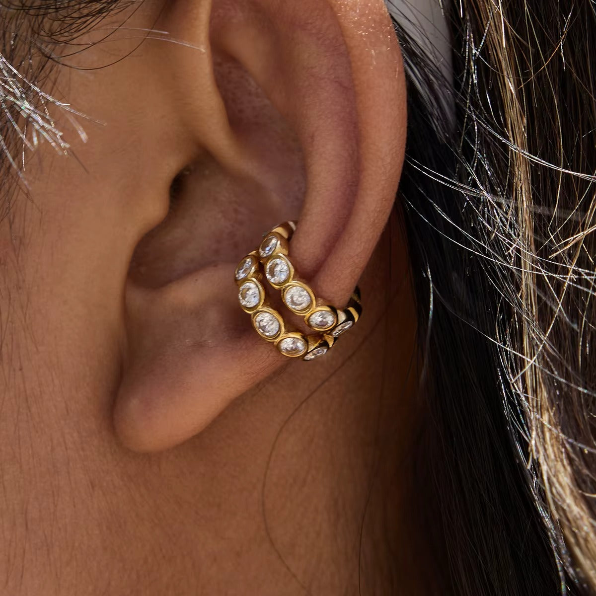 Two Nomad ear cuffs stacked on the ear, their textured gold bands each lined with bezel-set round crystals.
