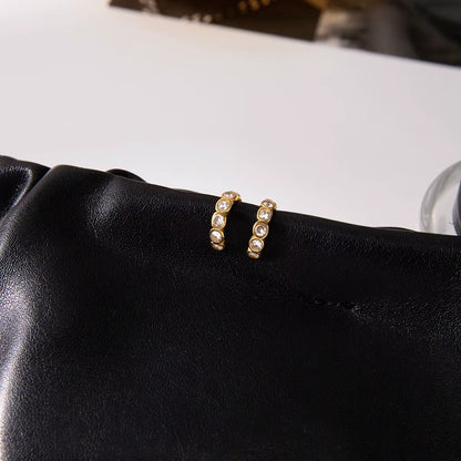 Nomad ear cuffs placed on black leather, shown close up with the bezel-set crystals lined along the curved gold band.