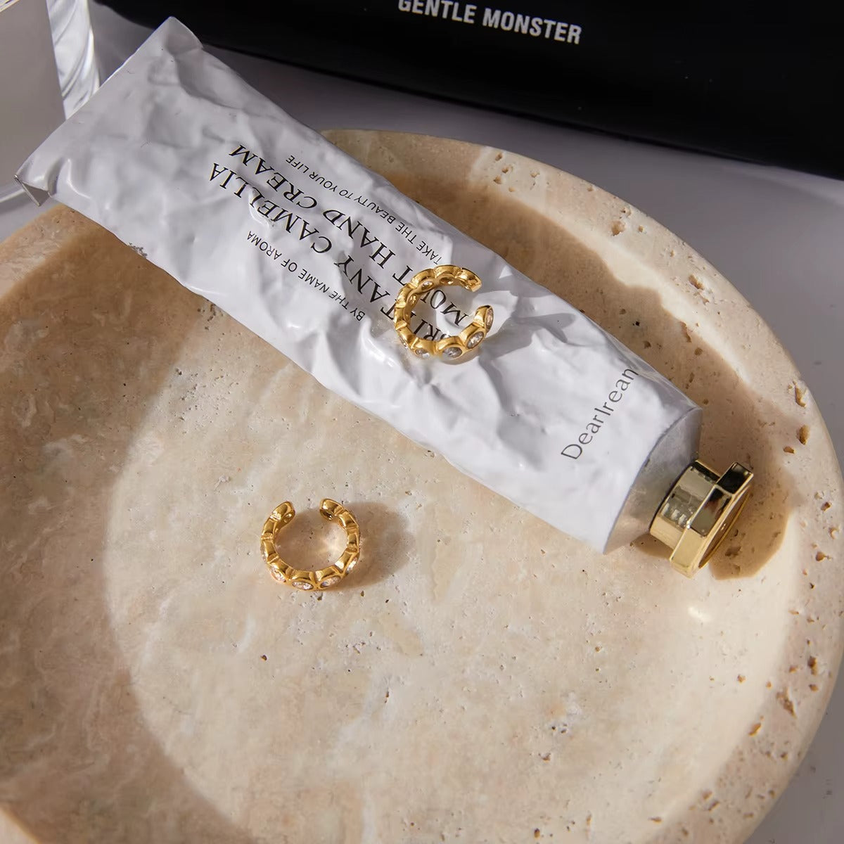 Nomad ear cuff styled in a flat lay with a hand cream tube, gold ring, and other accessories in a stone bowl.