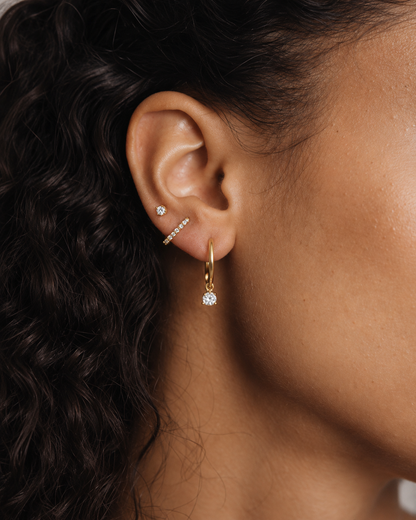 Model's ear wearing the gold Folie à Trois Noor SET stacked: a small stud, a pavé bar stud and a hoop with a dangling crystal.