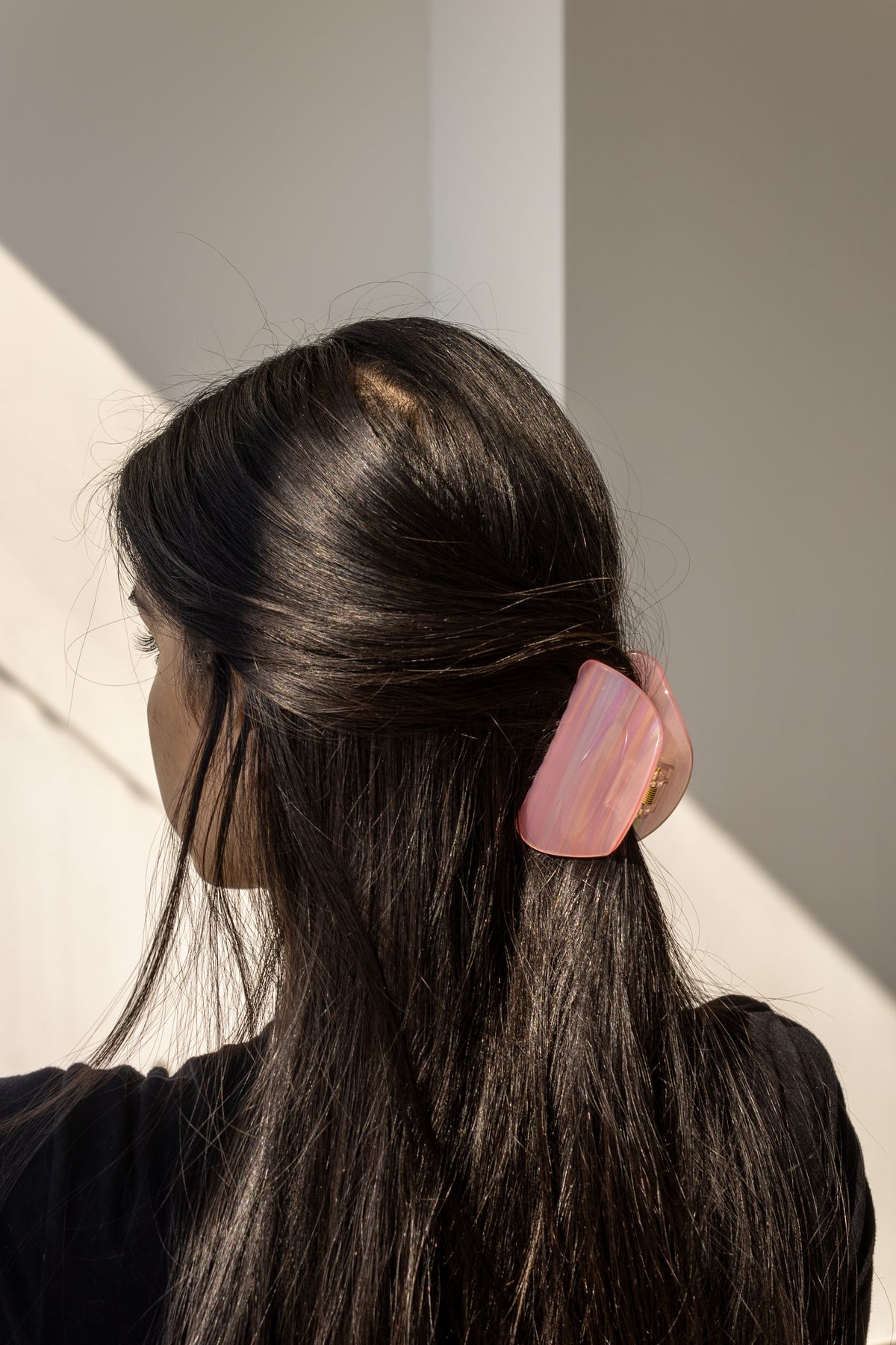 A woman wearing a solid smooth pink hair claw clip in her hair, back view in sunlight.
