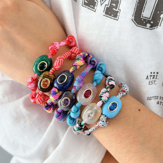 Wrist stacked with colourful Orchard BRACELETS: braided cords with gemstone charms in green, blue, purple, pink and white