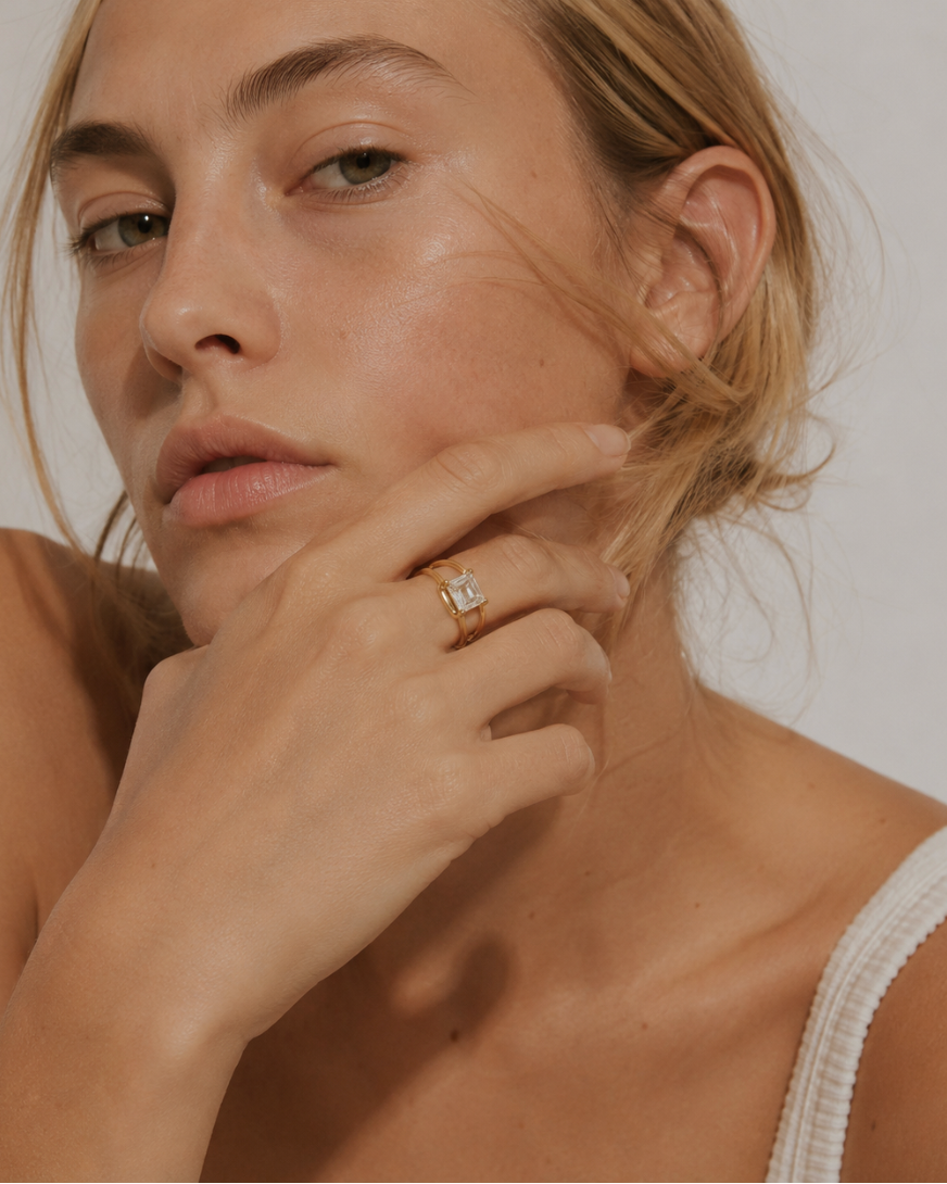 Model wears a gold Ovale RING with an emerald-cut white stone, hand raised to the chin — Folie à Trois wholesale jewelry