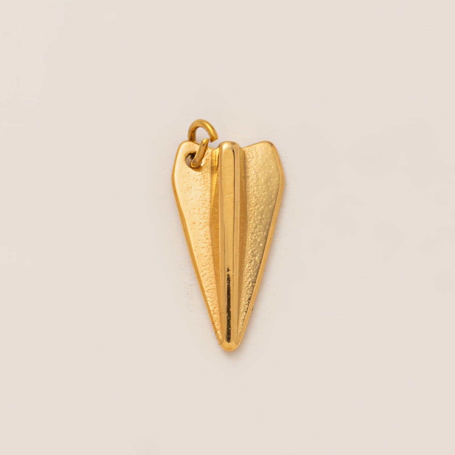 The Paper Airplane CHARM in gold, a folded airplane pendant with a matte finish, shown in close-up studio photography on cream.