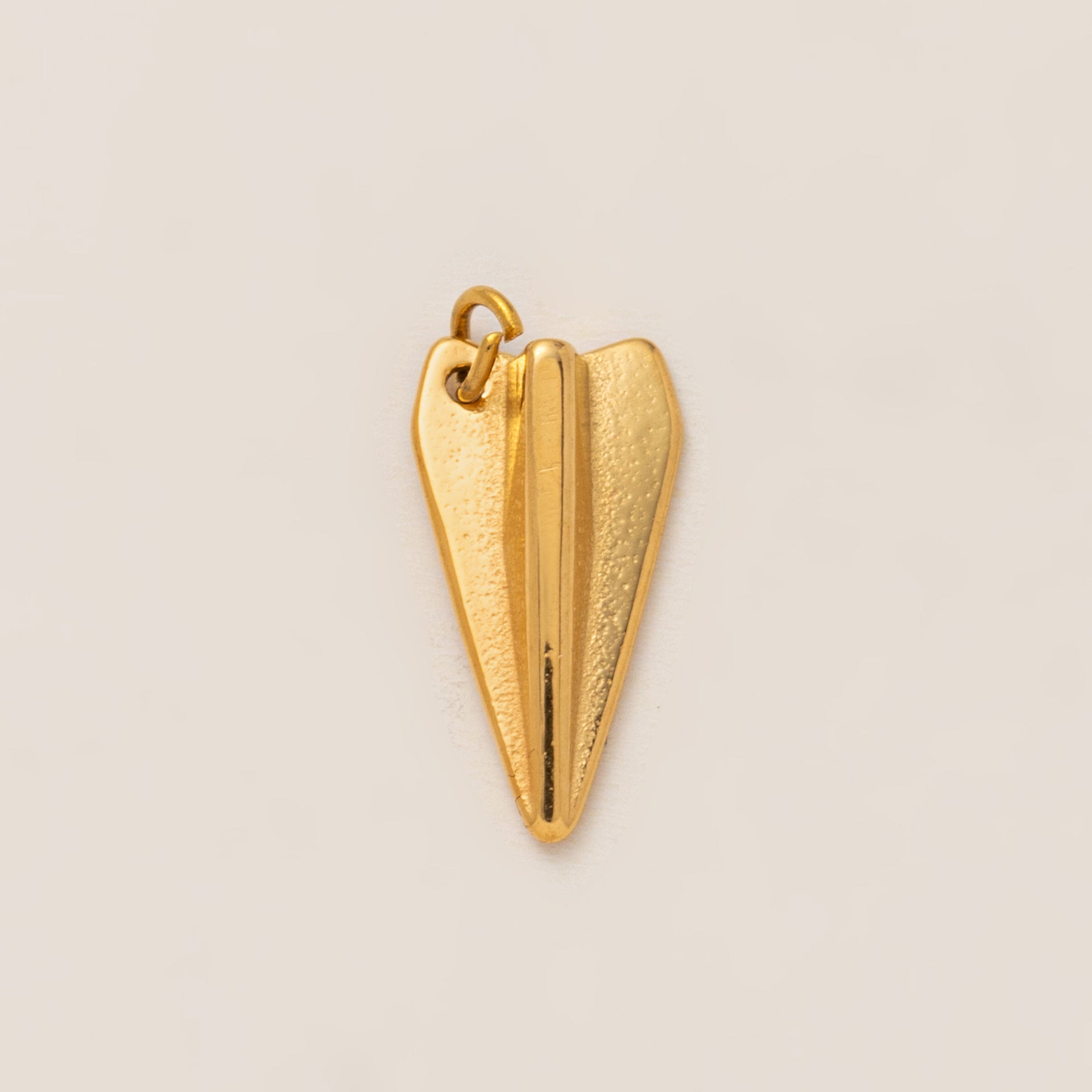 The Paper Airplane CHARM in gold, a folded airplane pendant with a matte finish, shown in close-up studio photography on cream.