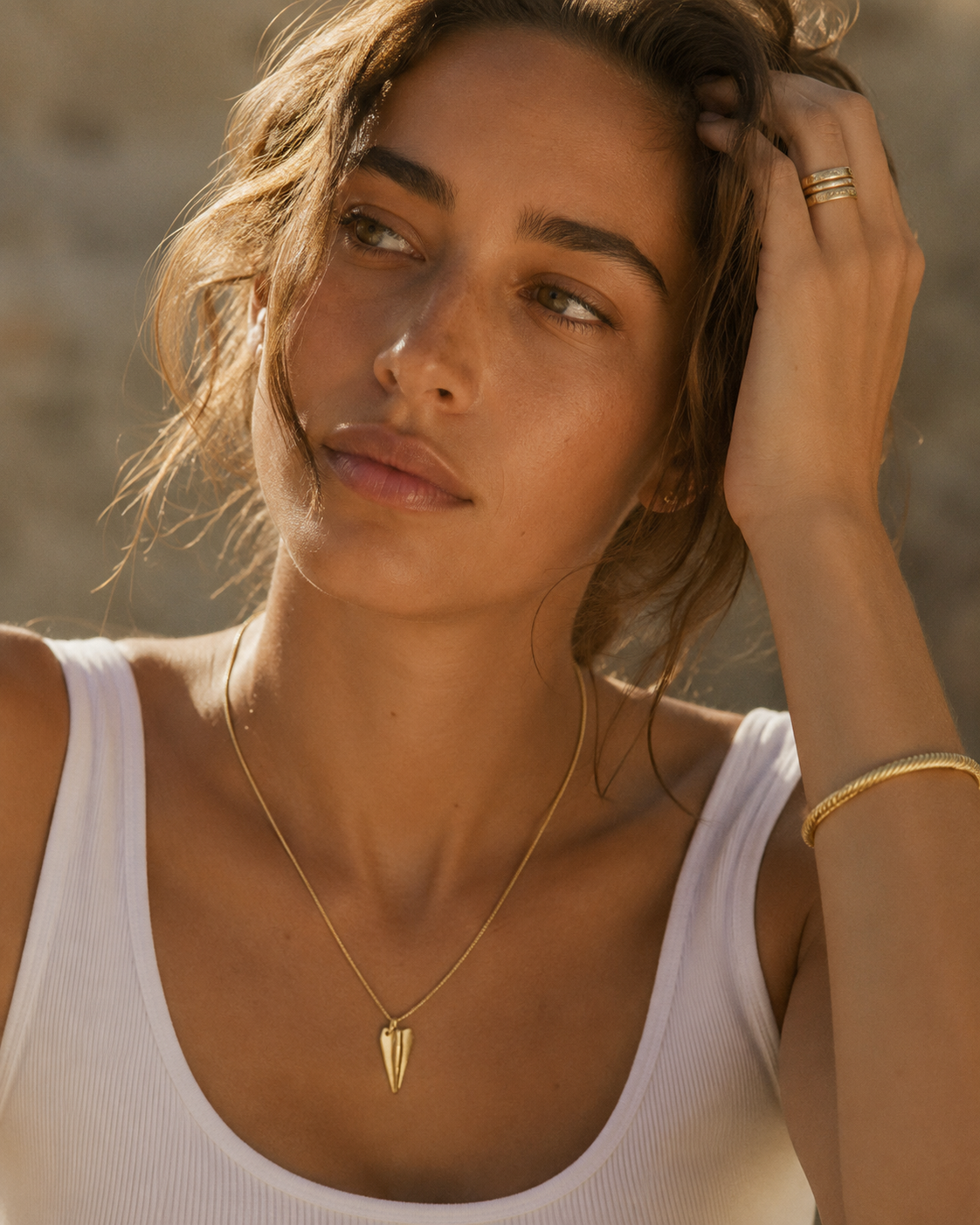 The Paper Airplane CHARM worn as a pendant on a fine gold chain necklace, resting at the neckline over a white tank top.