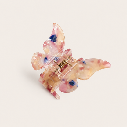 Papillon HAIR CLIP butterfly claw clip in translucent resin with pink, red and blue floral inclusions, on beige.