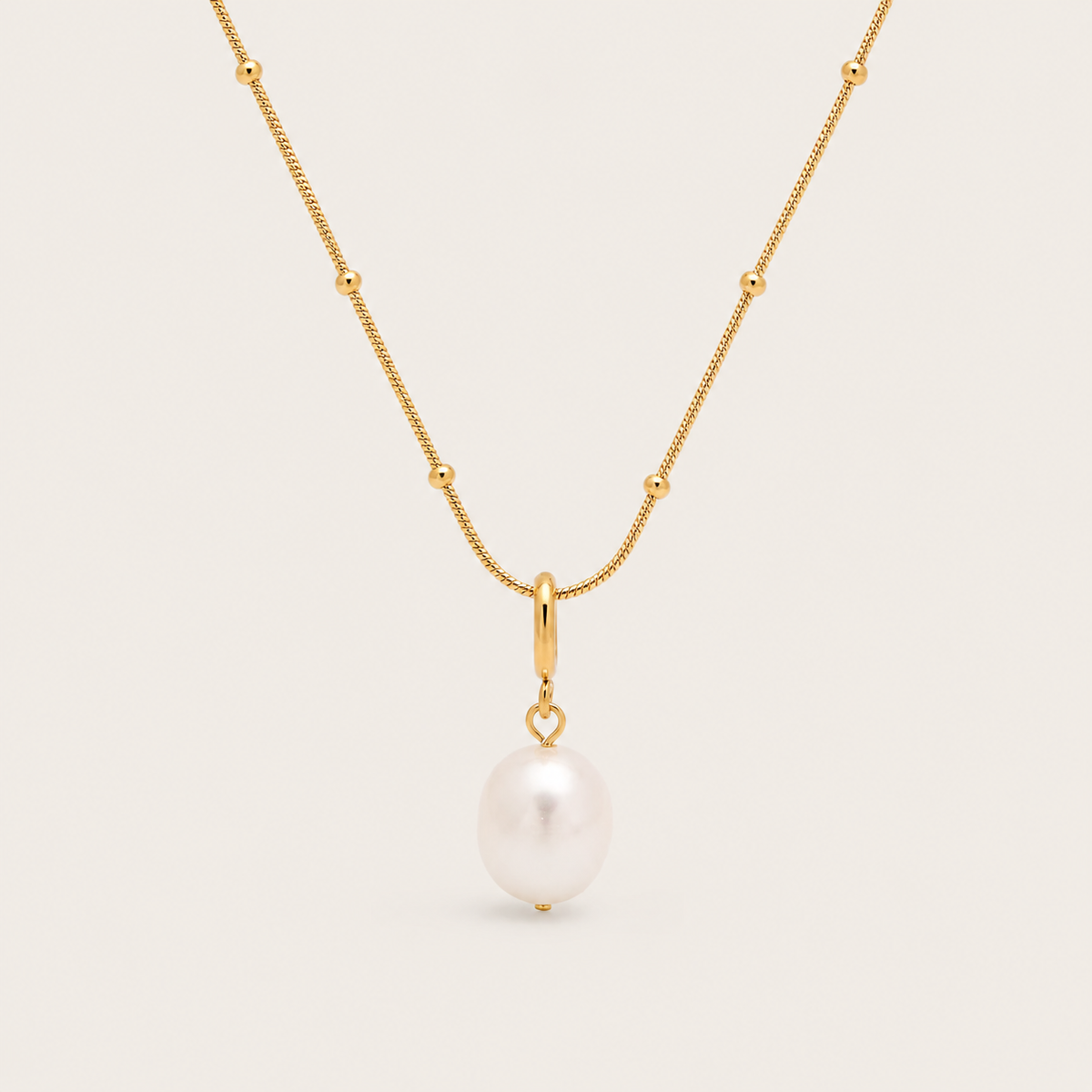 Gold beaded chain necklace with a single freshwater pearl drop from the Pearl Me NECKLACE design, laid flat on beige.
