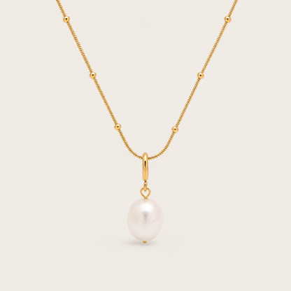 Gold beaded chain necklace with a single freshwater pearl drop from the Pearl Me NECKLACE design, laid flat on beige.