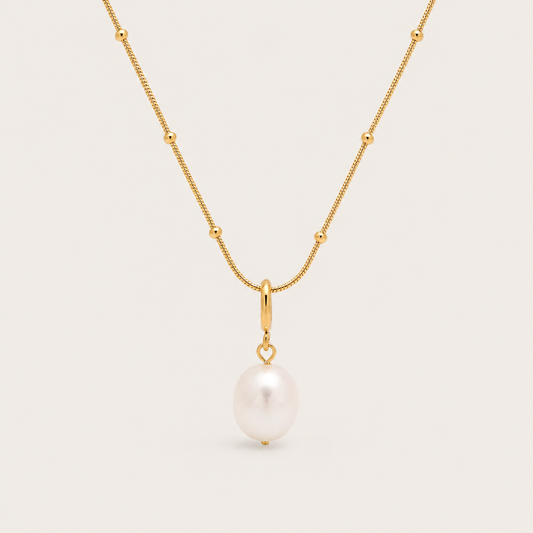 Gold beaded chain necklace with a single freshwater pearl drop from the Pearl Me NECKLACE design, laid flat on beige.