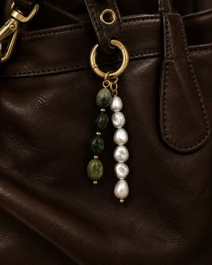 Folie à Trois Perla BAG CHARM in green jade and white pearl strands, hanging from a gold hoop clasp on a dark brown leather bag.