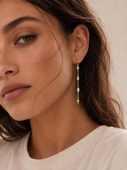 Close-up of a model wearing the gold Perla Luna EARRINGS, a long chain drop set with four freshwater pearls.
