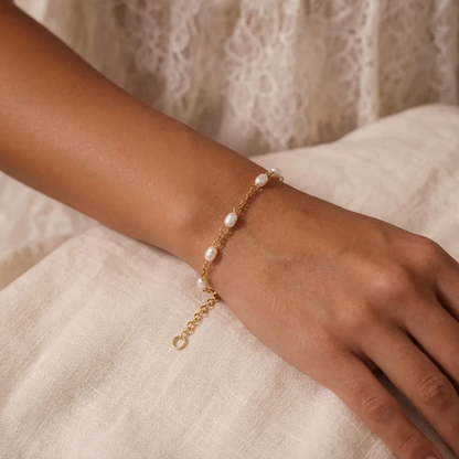 Perle BRACELET worn on the wrist with pearls catching the light, paired with a lace-trimmed cream dress in a close-up shot.