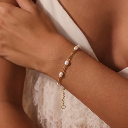 Perle BRACELET worn on the wrist with pearls along a fine gold chain, shown close-up with arms crossed over a cream dress.