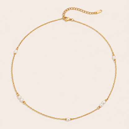 Gold satellite chain necklace with small pearl stations from the Perle NECKLACE design, laid flat on beige.