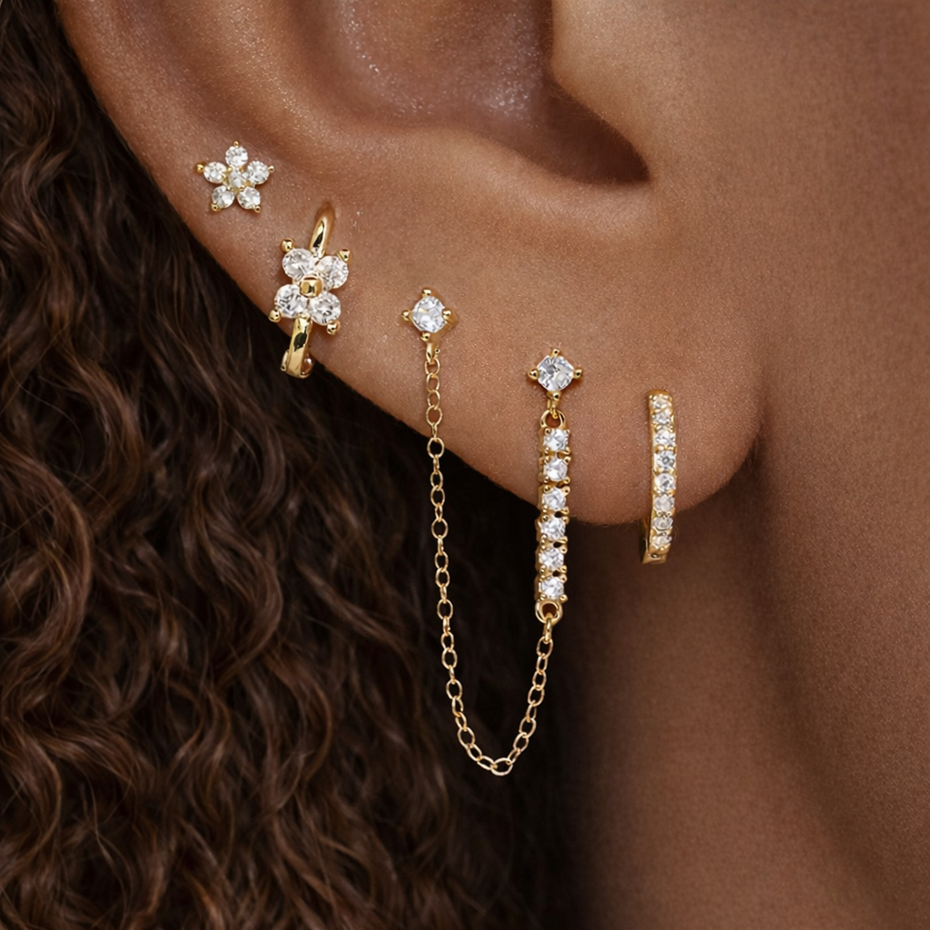 Pixie Set worn stacked on the ear, mixing a flower stud, huggie hoop, and a draped chain connecting two crystal studs.