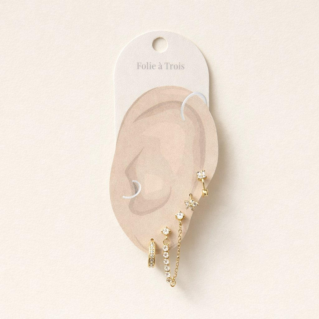 Pixie Set displayed on a Folie a Trois ear-shaped card, arranging the gold flower stud, hoop, and chain-linked studs for styling.
