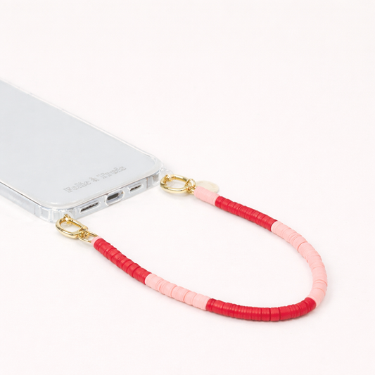 Red and pink heishi bead Poppy SHORT PHONE CORD clipped to a clear phone case with gold hardware.