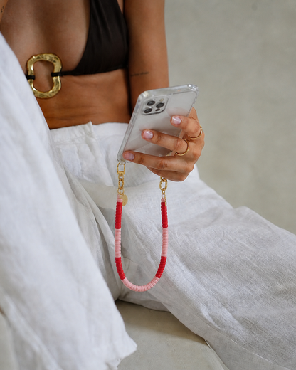 Woman holding a phone case attached to a red and pink heishi bead Poppy SHORT PHONE CORD.
