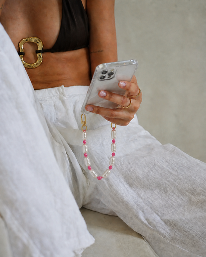 Woman holding a clear phone case attached to the white pearl and pink bead Posy Pearl SHORT PHONE STRAP.