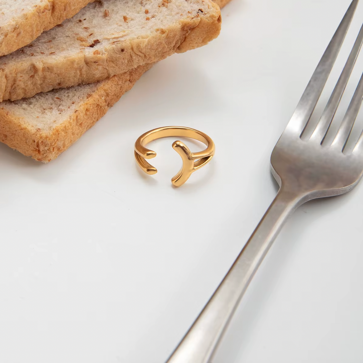 Styled flatlay of the open gold branching Power Play RING resting beside bread slices and a fork on a white surface.