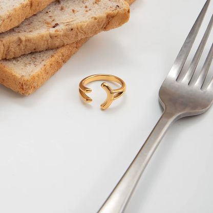 Styled flatlay of the open gold branching Power Play RING resting beside bread slices and a fork on a white surface.
