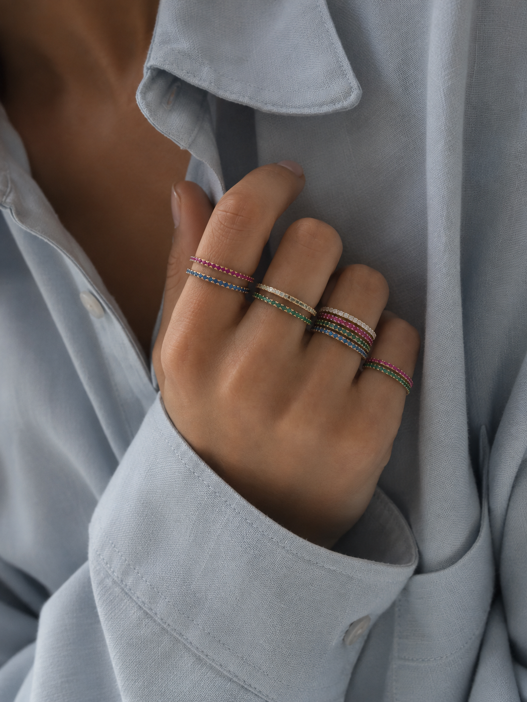 A hand in a light blue shirt stacks four Prisma RING colorways in pink, white, green and blue — Folie à Trois wholesale stacking rings