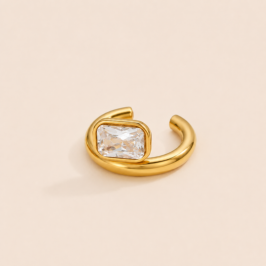 The Procida EAR CUFF in a flat lay, a gold open cuff set with a clear rectangular gem, shown on a soft beige background.