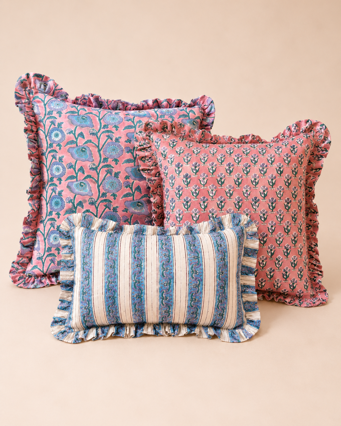 Three ruffled block-print cushions in pink floral and blue stripe patterns styled together, representing the Razia, Yavi and Taj cushions.